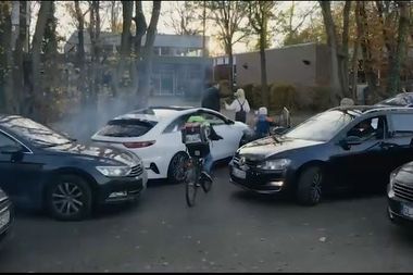 Screenshot aus dem Kurzfilm „Wir machen uns mobil – auch ohne Auto!“ zeigt parkende Autos vor der Schule, dazwischen auf dem Fahrrad und zu Fuß gehende Schulkinder. Foto: Grundschule Hogenkamp.