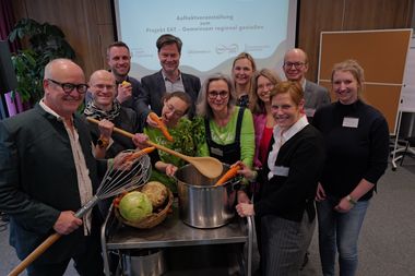 Zu sehen sind Personen, die den Auftakt des Verbundprojektes EAT begehen. Sie stehen rund um einen Servierwagen mit Gemüse und Töpfen. Foto: Jörg Hemmen