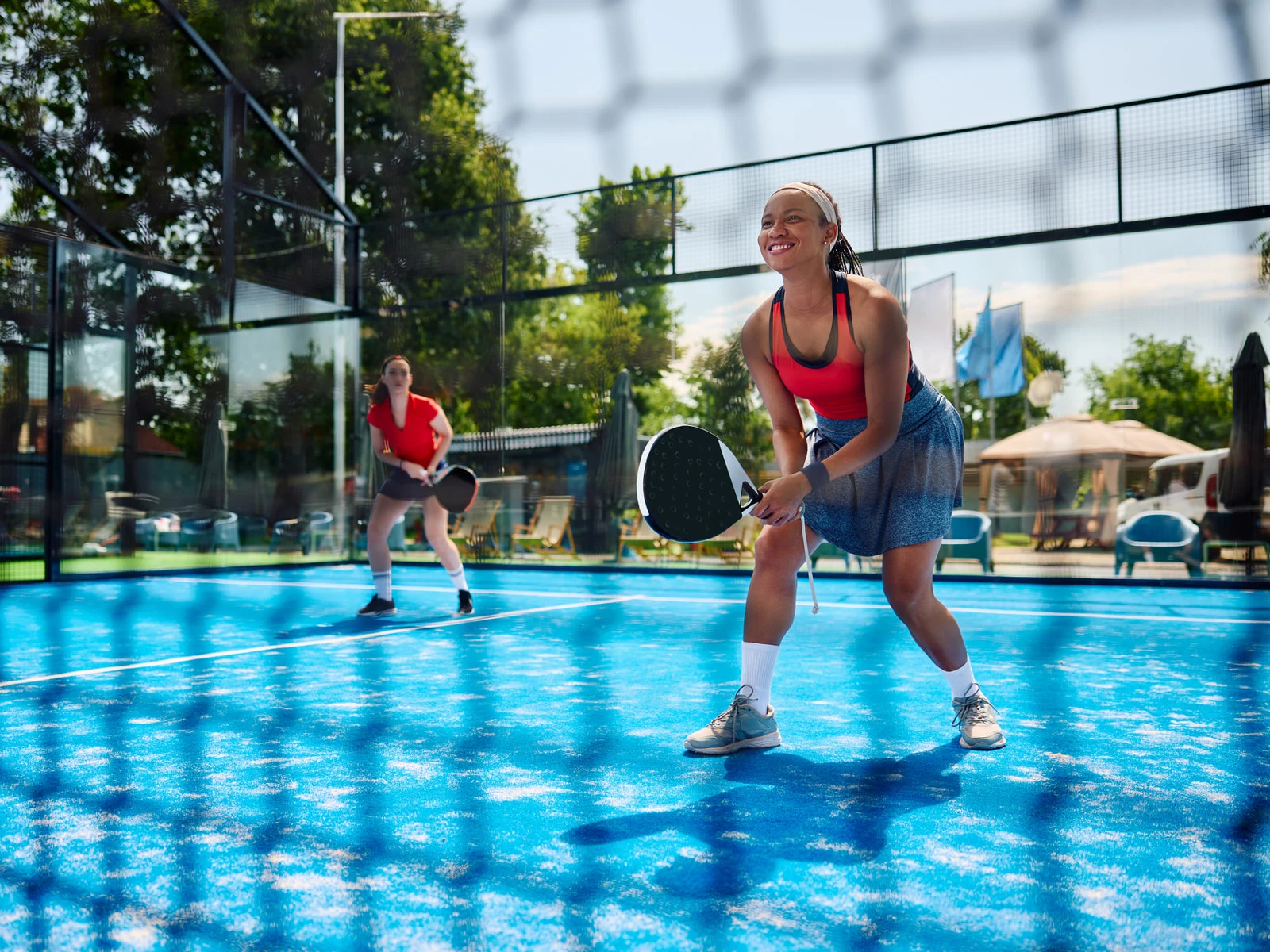 Padel Court im Freien: Spielerinnen auf blauem Padel-Kunstrasen hinter der Glaswand