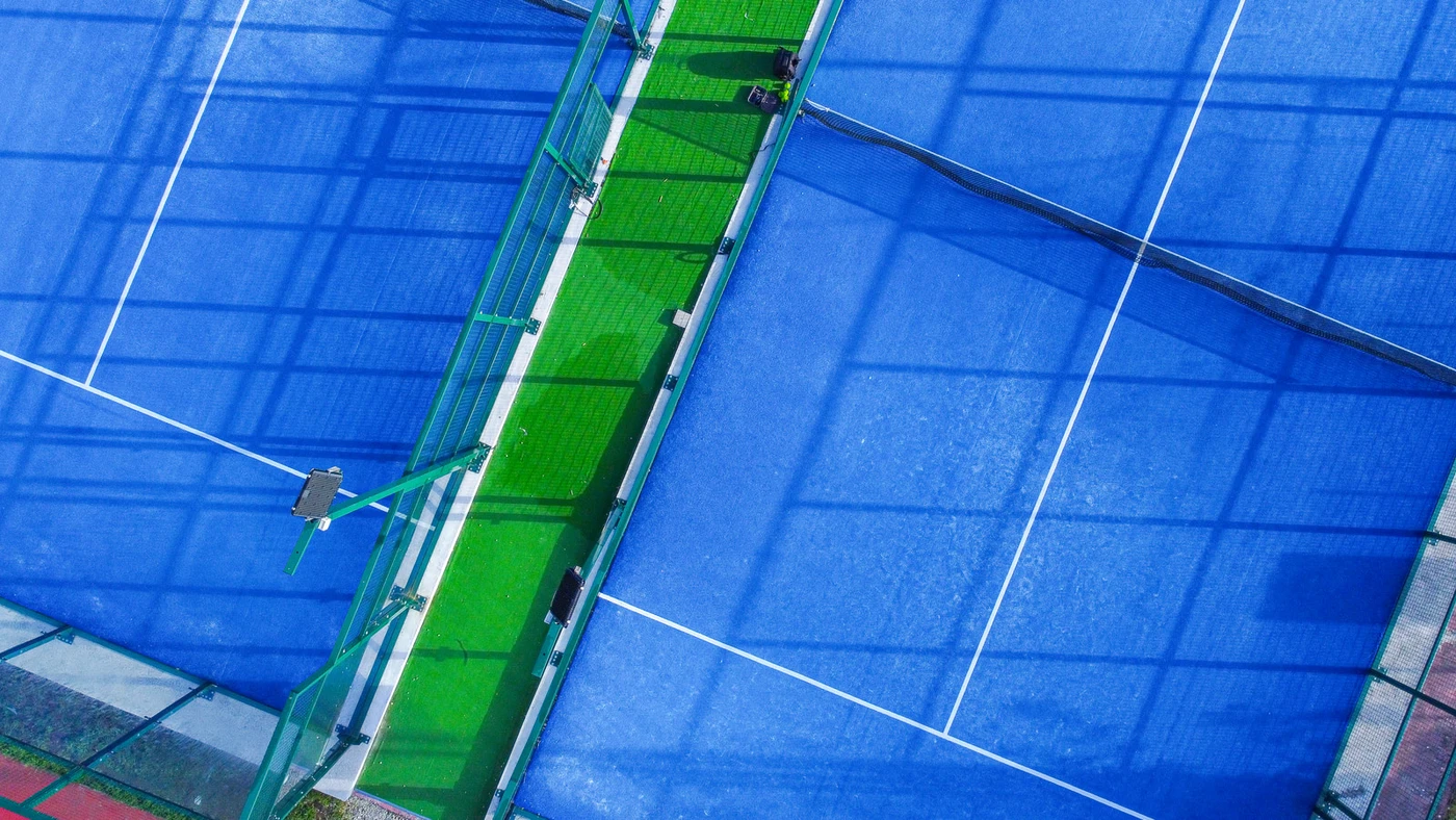 Zwei Padel Courts von oben mit blauem Kunstrasen, weißen Linien und grünem Gang dazwischen