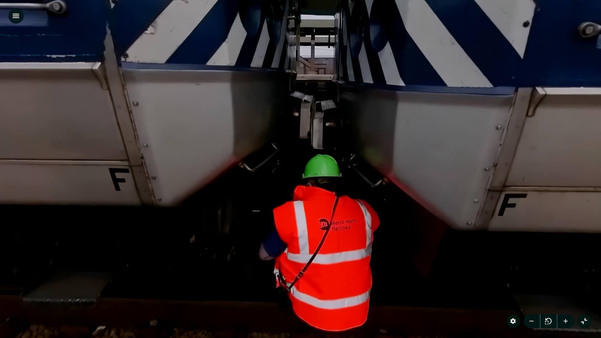 Worker in high-visibility gear and green helmet inspects the coupling between two trains.