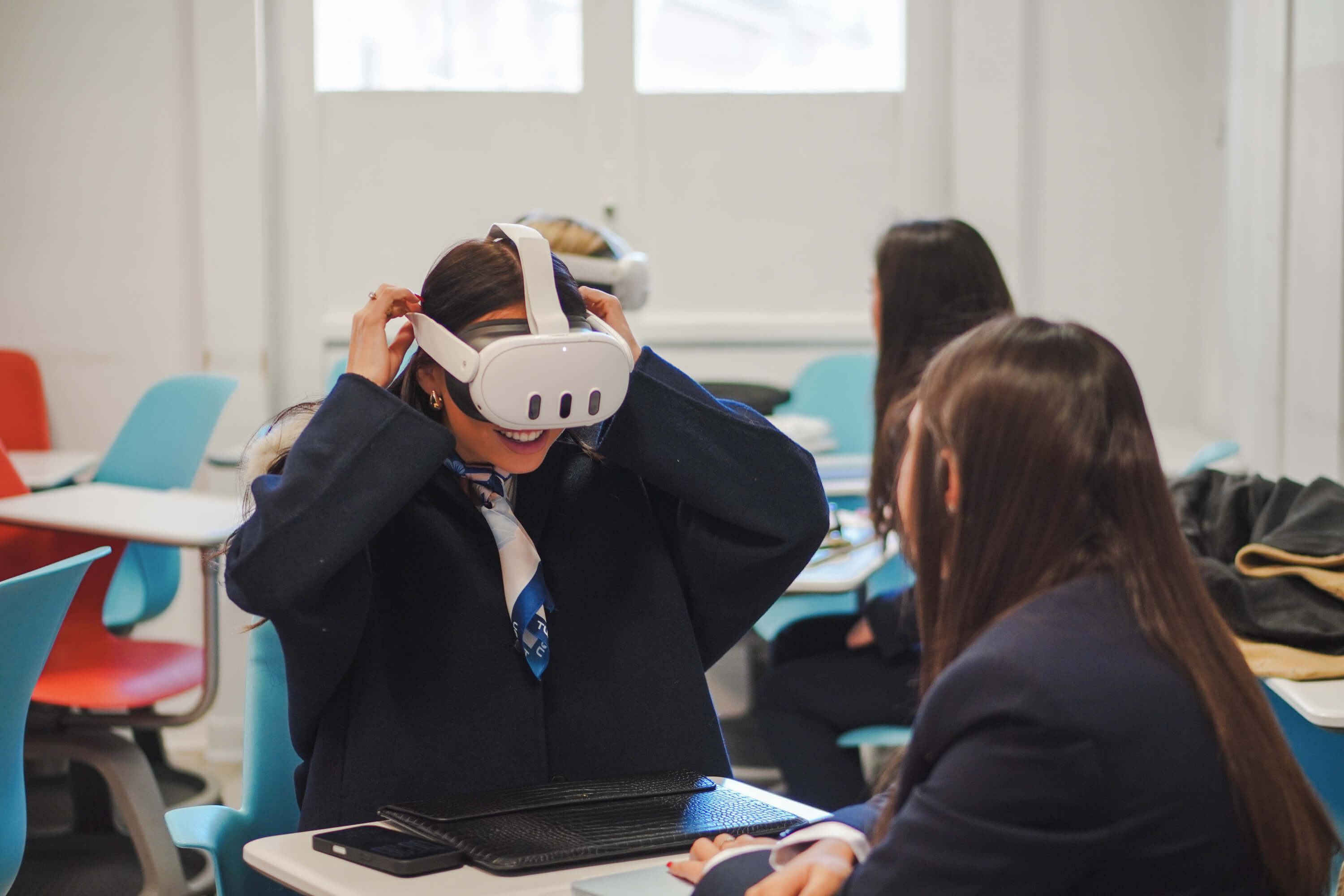 A woman in formal attire, wearing a VR headset, sits with a controller in her hand.