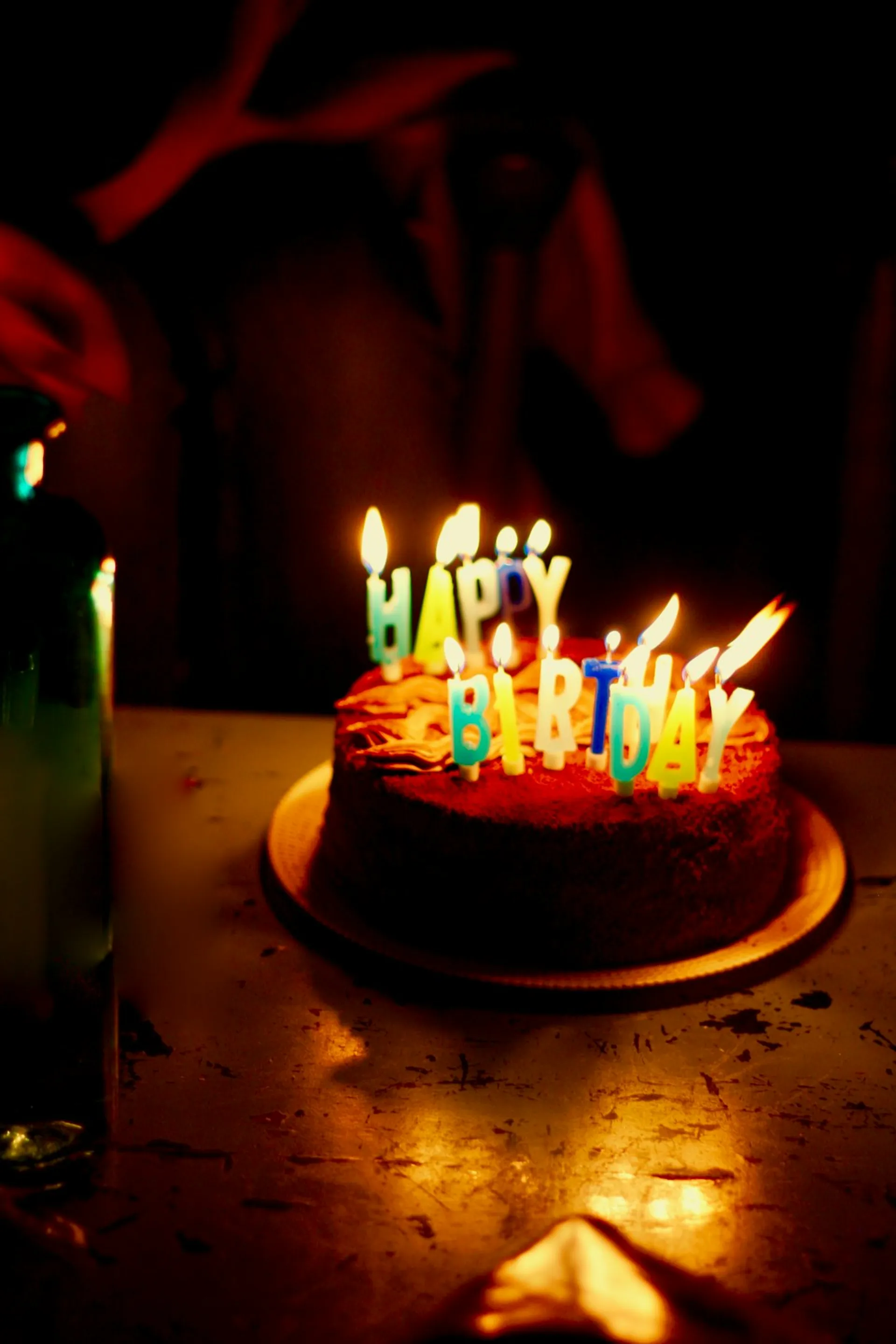 Lit birthday candles spelling out a message on a cake in a dark room