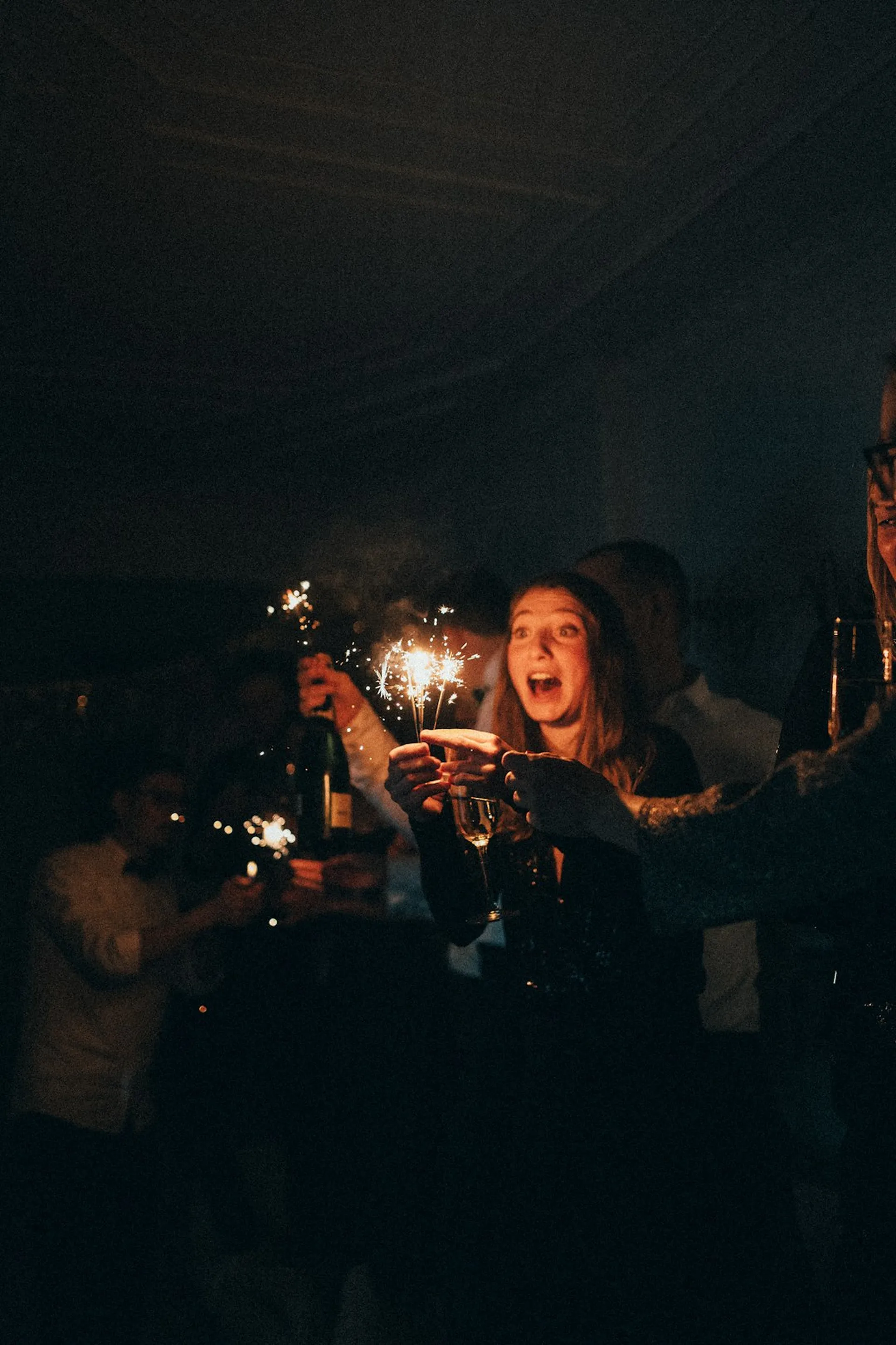 A person holding sparklers at a party, others celebrating behind