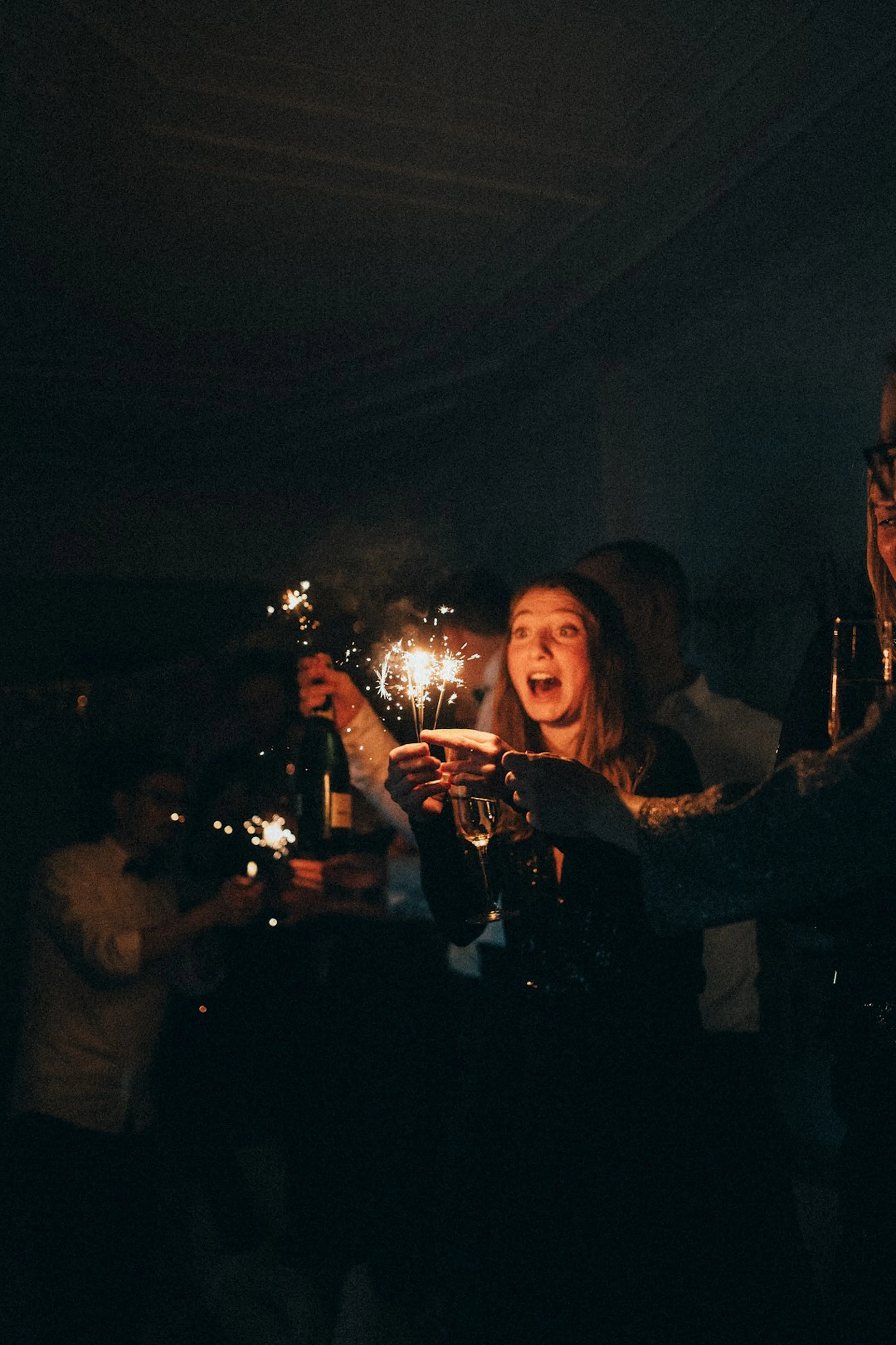 A person holding sparklers at a party, others celebrating behind