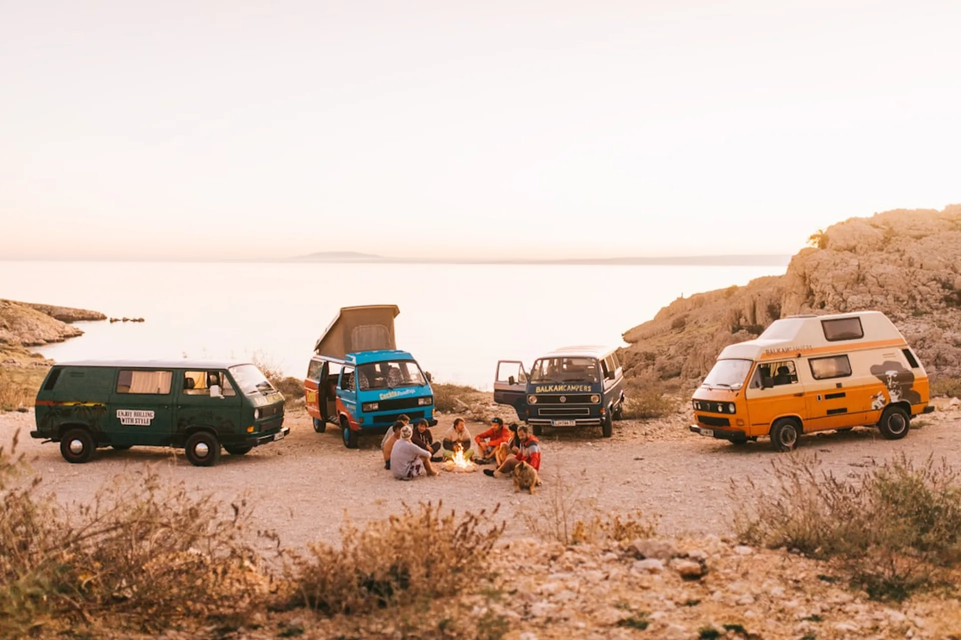 Friends around a campfire beside their campervans at sunset on a group trip