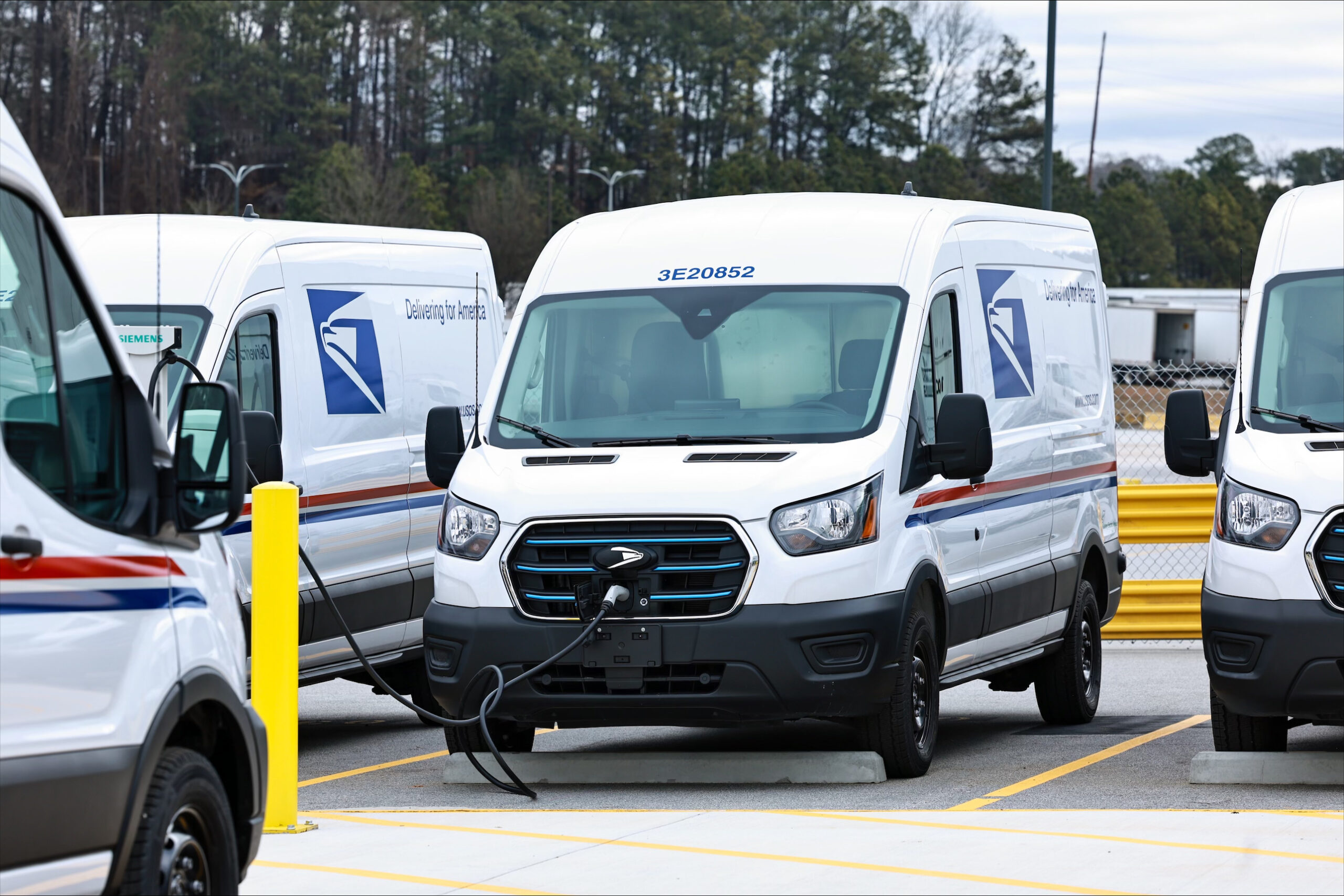 USPS electric delivery vans with fleet graphics charge at the South Atlanta Sorting and Delivery Center during the 2024 EV fleet launch.