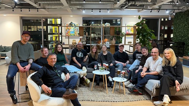 A group of people sitting on couches and chairs in a modern, well-lit room with plants and decorative shelves in the background.