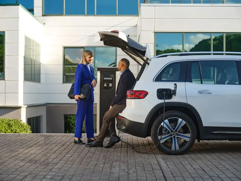 Man and woman chating on boot of the car while charging
