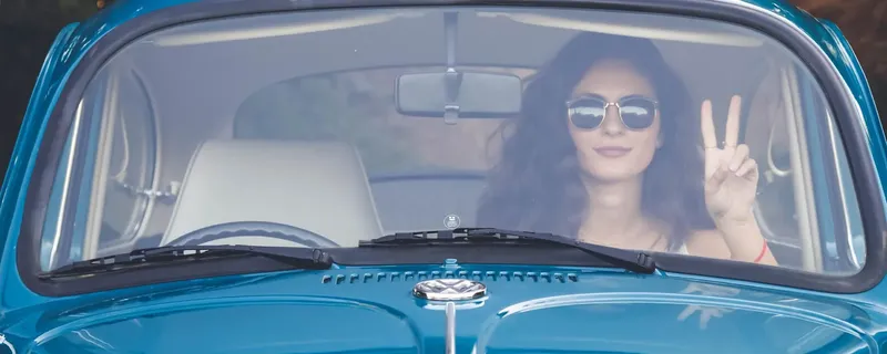 Woman in blue car doing V sign