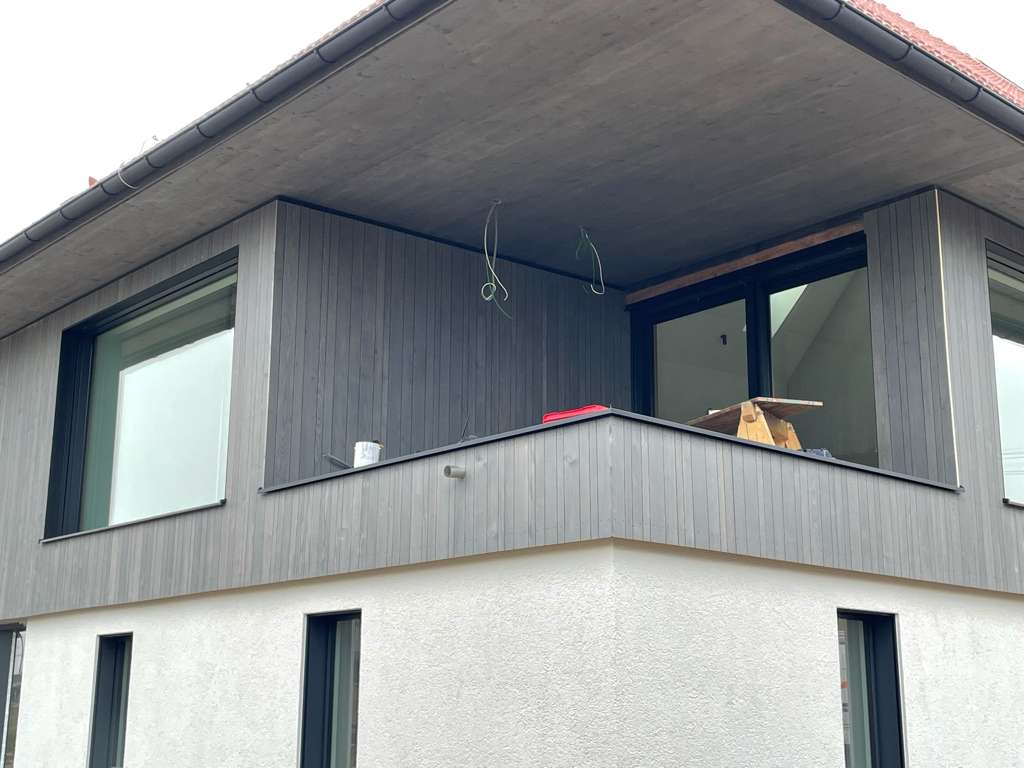 Außenansicht eines Balkonbereichs ohne Gelände mit Holzpanelen an der Fassade.