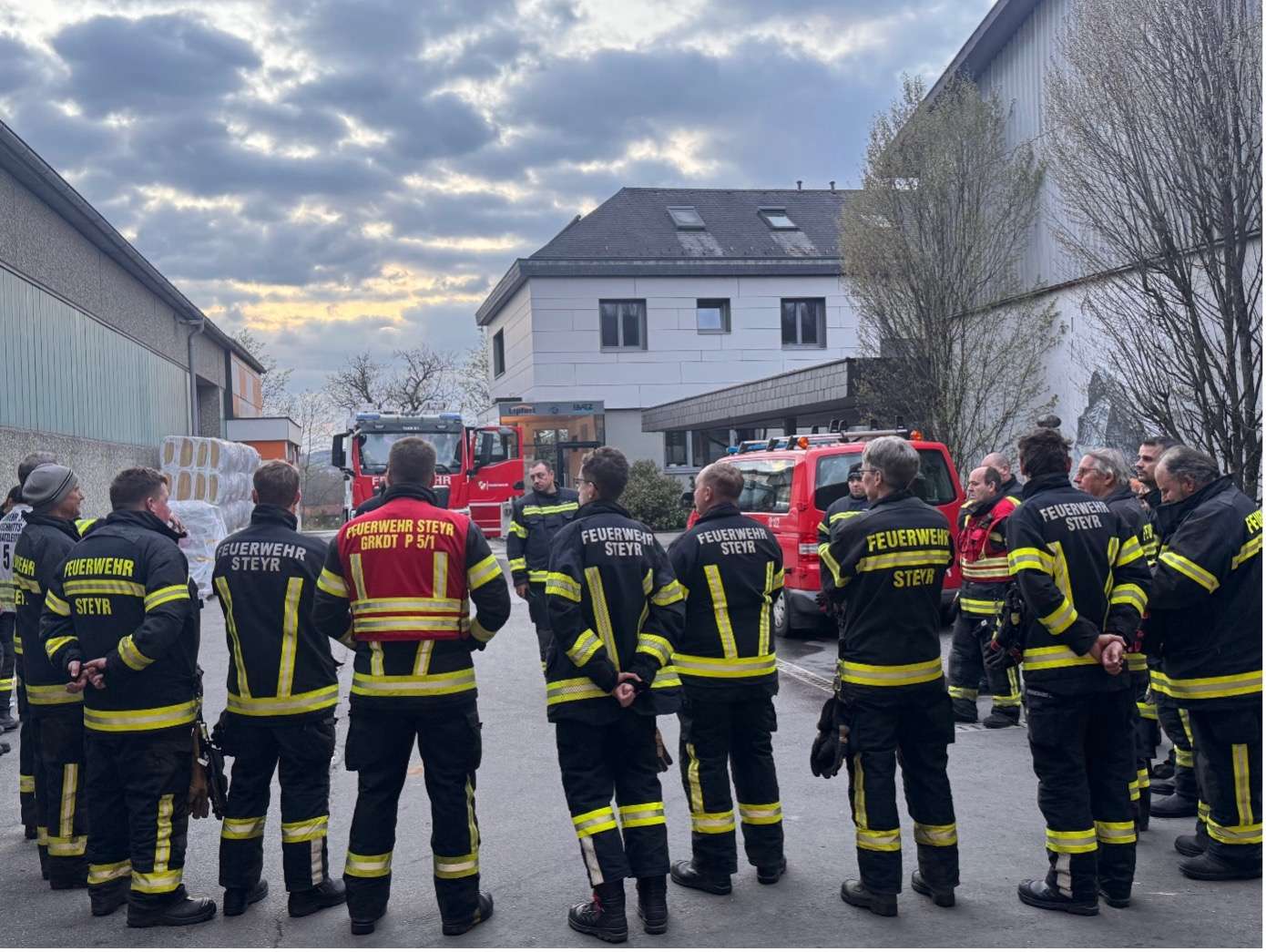 Mehrere Männer in Feuerwehrkleidung von hinten blicken auf die Kommandofahrzeuge auf dem Lipfert Betriebsgelände.