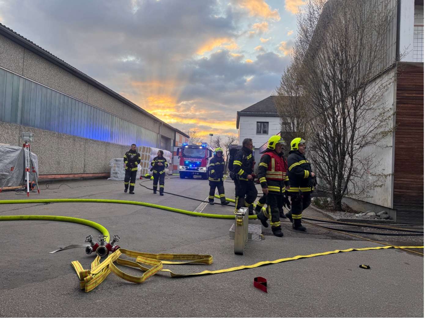 Mehrere Personen in Feuerwehrkleidung mit Löschschlauch im Vordergrund und Kommandowagen im Hintergrund.