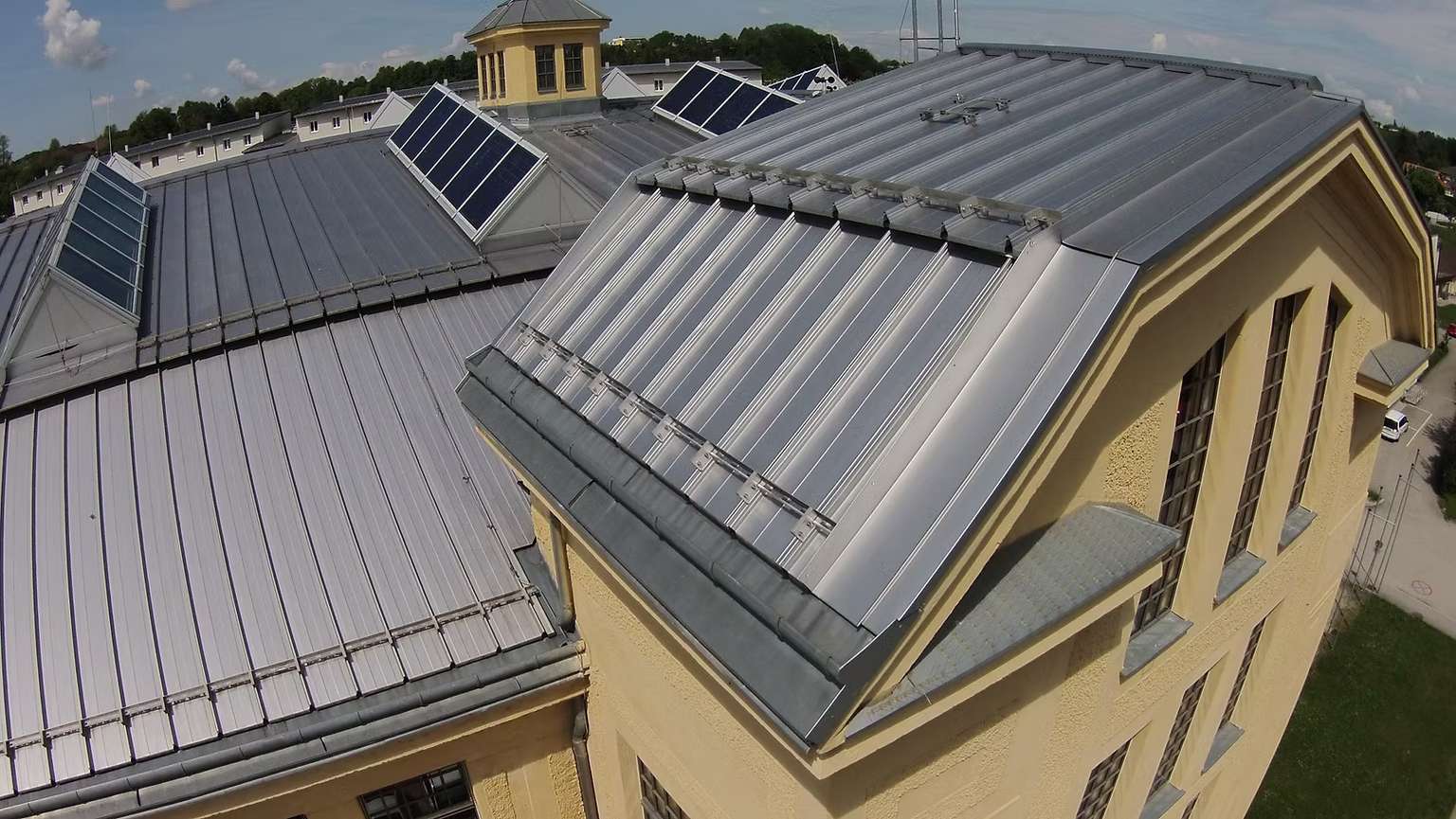 Luftansicht von Wohnkomplexen mit gelber Fassade und grauem Dach mit PV-Panelen.