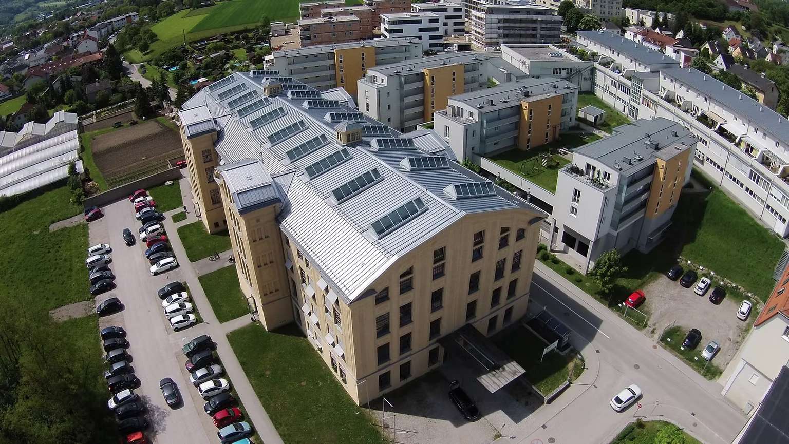 Luftansicht von Wohnkomplexen mit gelber Fassade und grauem Dach mit PV-Panelen.