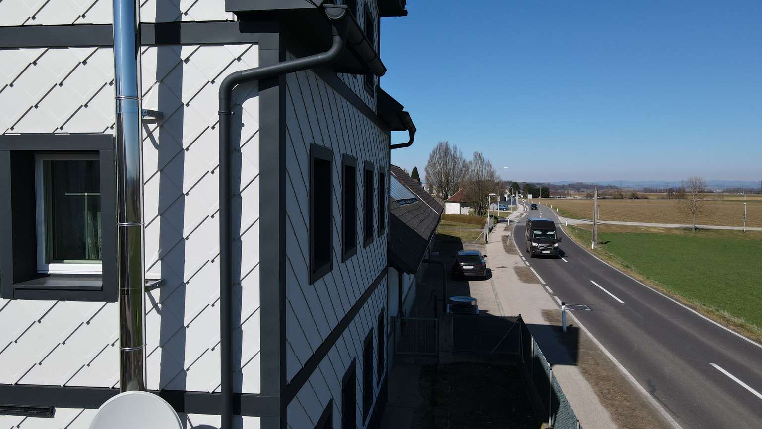 Eckansicht eines Gebäudes an einer Straße mit Fassade und schwarz umrandeten Fenstern und Gebäudeecken.