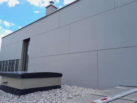 Fassade in grauen Platten aufgenommen von Dachterasse mit Steingrund.