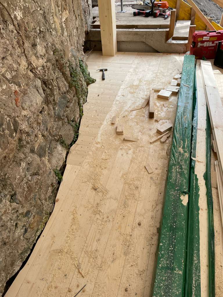 Erbauter Holzboden an Felswand angrenzend mit Werkzeug und Holzbalken sowie Holzschutt.