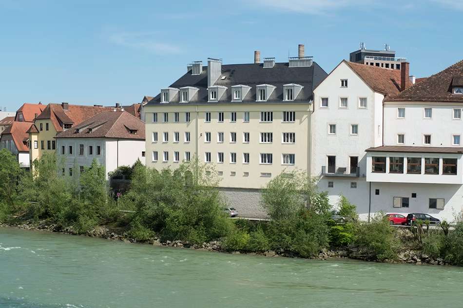 Ansicht einer Hausreihe am Wasser mit Bäumen am Ufer.