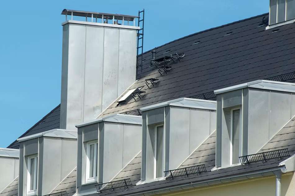 Dach mit vier Fenster und hohem silbernem Kaminausgang.
