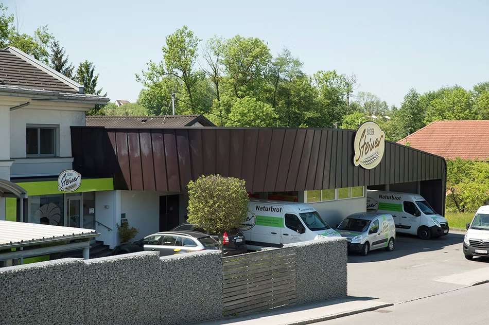 Steiner Firmengebäude mit Firmenautos und Steinzaun.