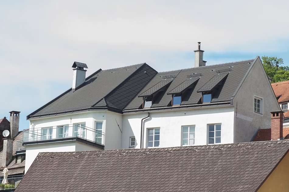 Weißes Haus mit Balkon und dunkelgrauem Haus.