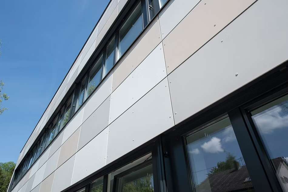 Nahansicht einer Fassade aus mehreren grauen und beigen Platten mit Fensterreihen.