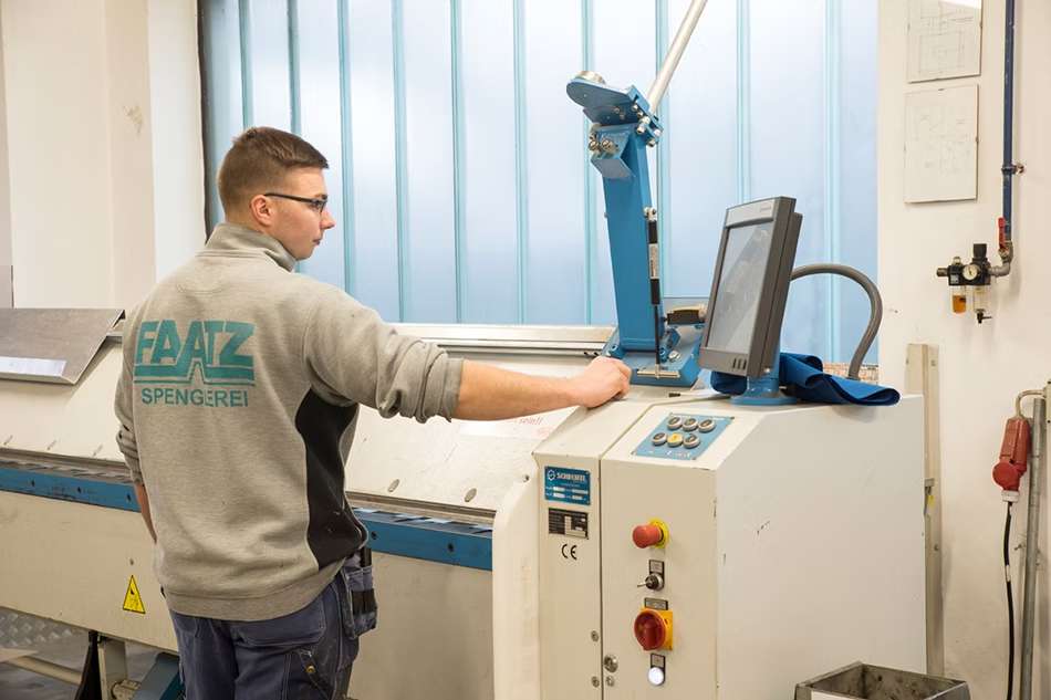 Mann in Arbeitskleidung steht an Maschine und blickt auf Bildschirm.