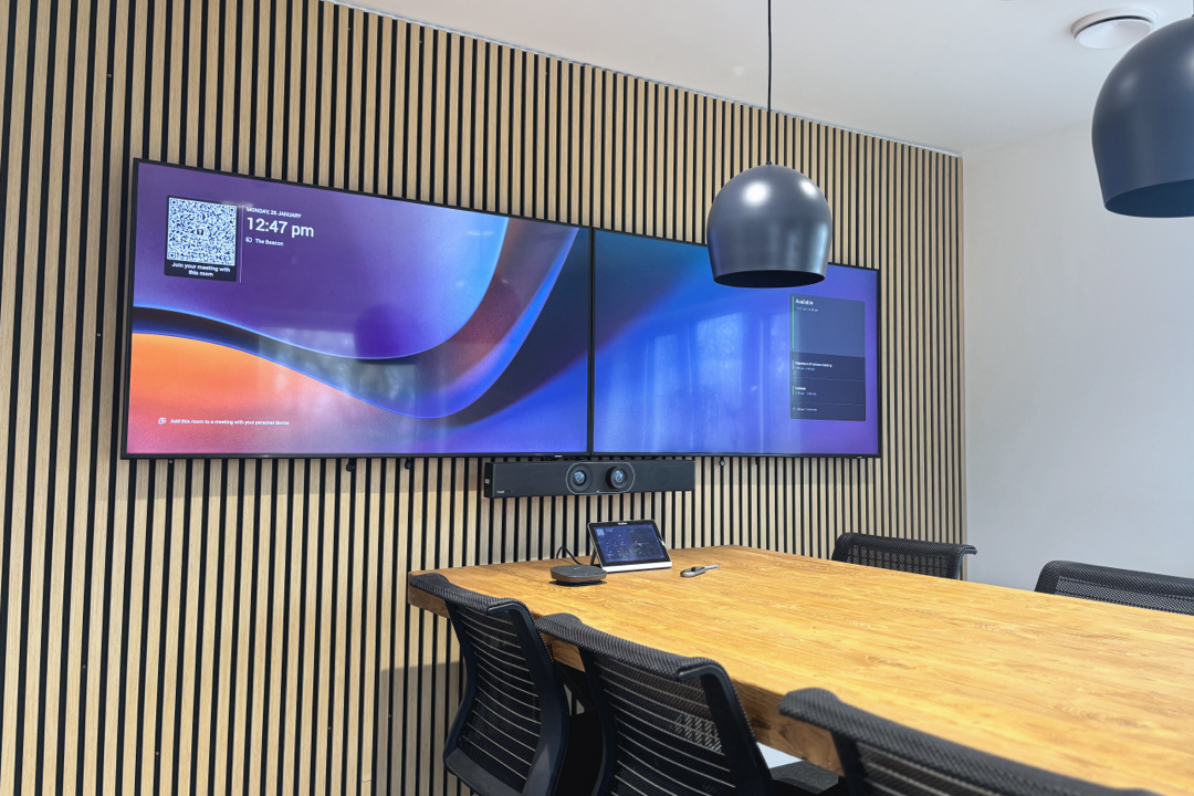 A meeting space with desk, duel screens and video conferencing equipment.