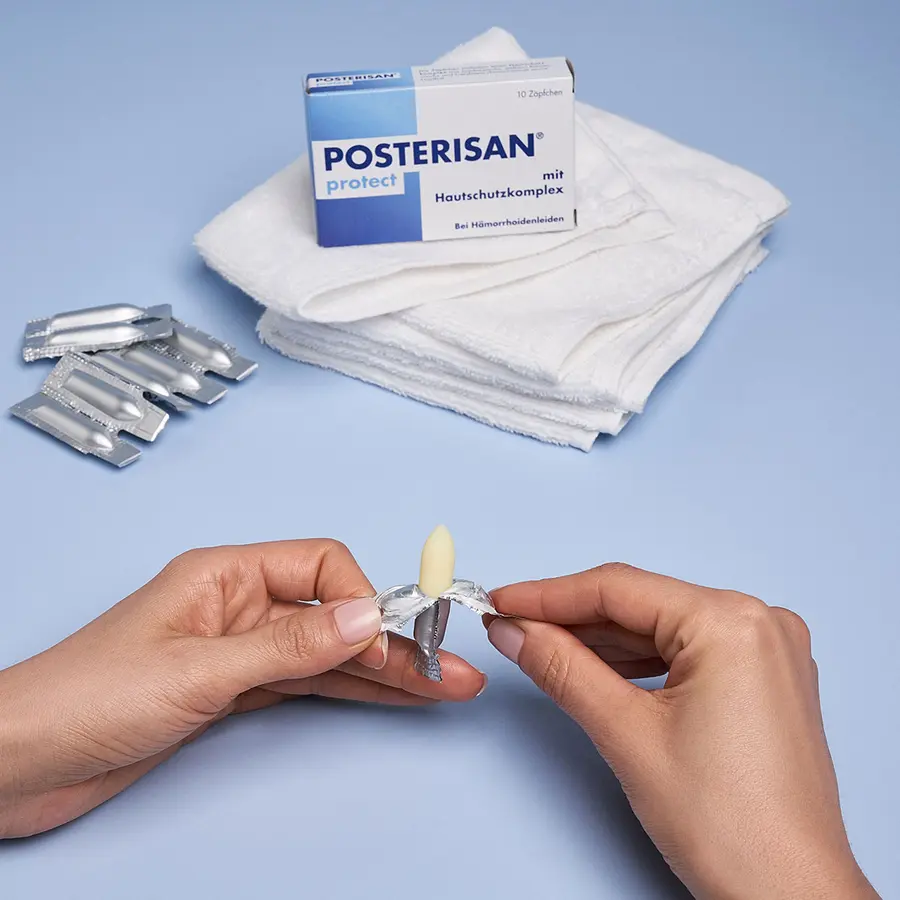 Hände öffnen ein Posterisan protect Zäpfchen vor der Produktpackung und weißen Tüchern
