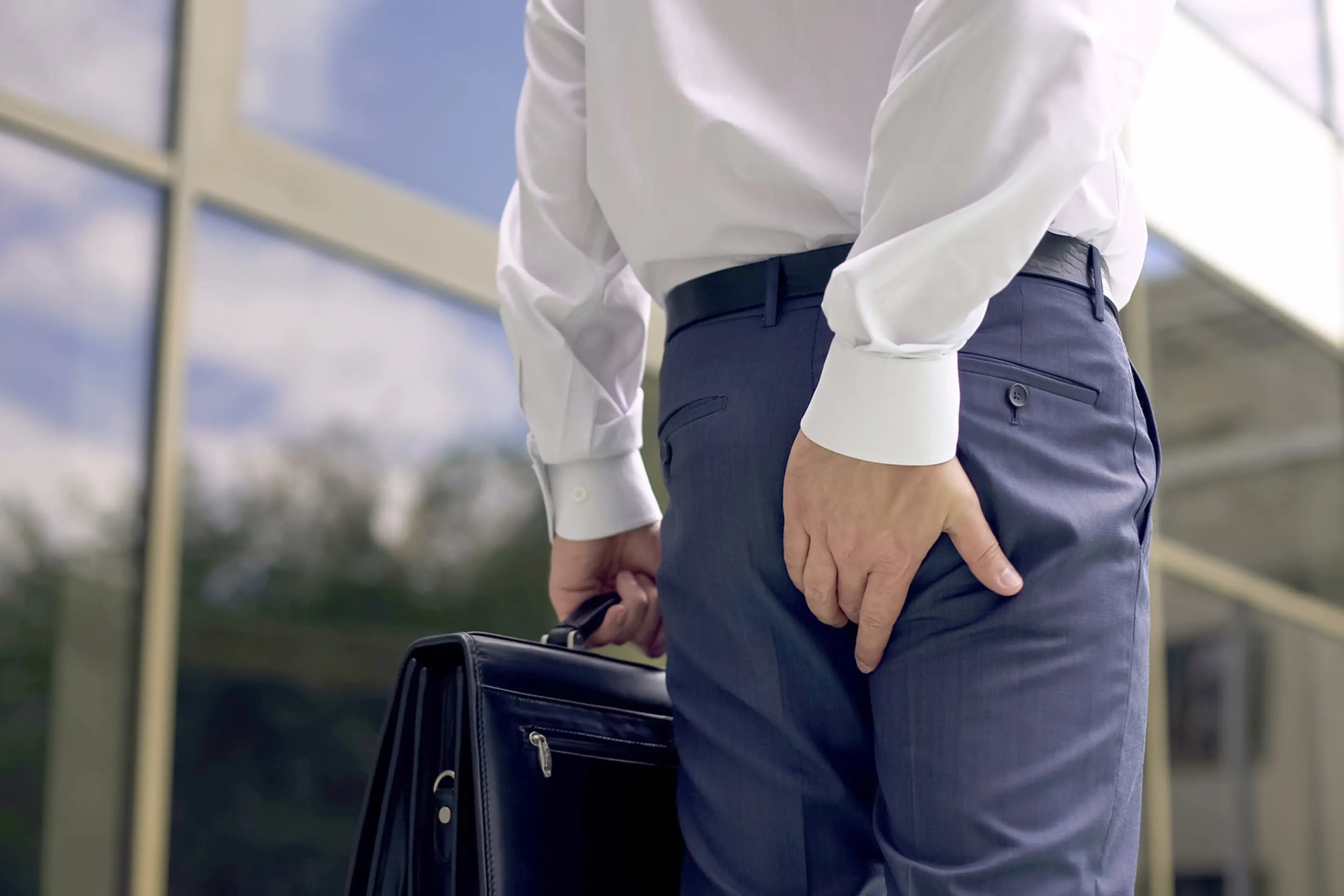Person in Businesskleidung hält eine Aktentasche und fasst sich an das Gesäß.