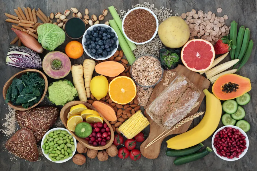 Verschiedene gesunde Lebensmittel wie Obst, Gemüse, Nüsse, Vollkornbrot, Haferflocken und Samen auf einem Tisch angerichtet