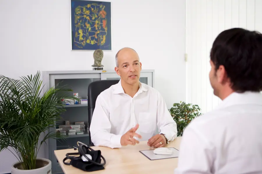 Arzt und Patient sitzen sich in einer Praxis gegenüber und führen ein Diagnose-Gespräch über Hämorrhoiden.