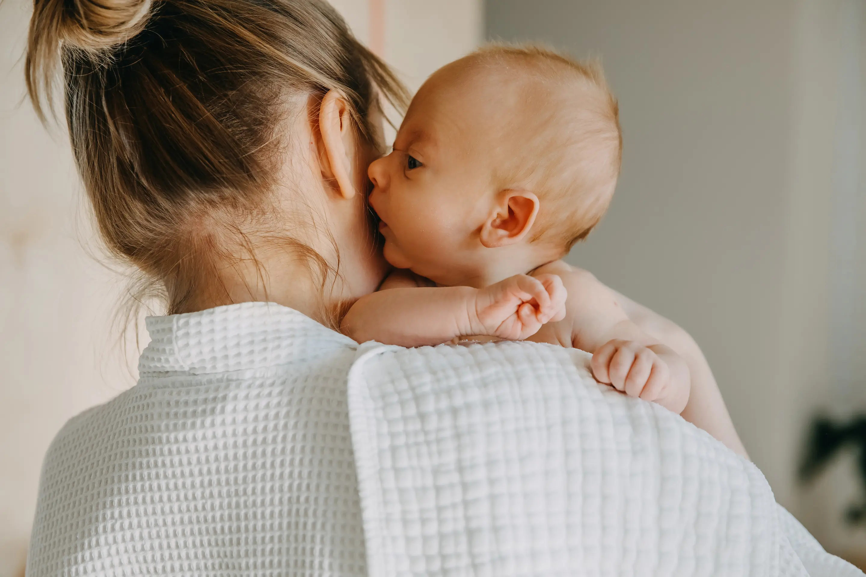 Mutter hält ihr Baby im Arm und trägt es nah am Körper.
