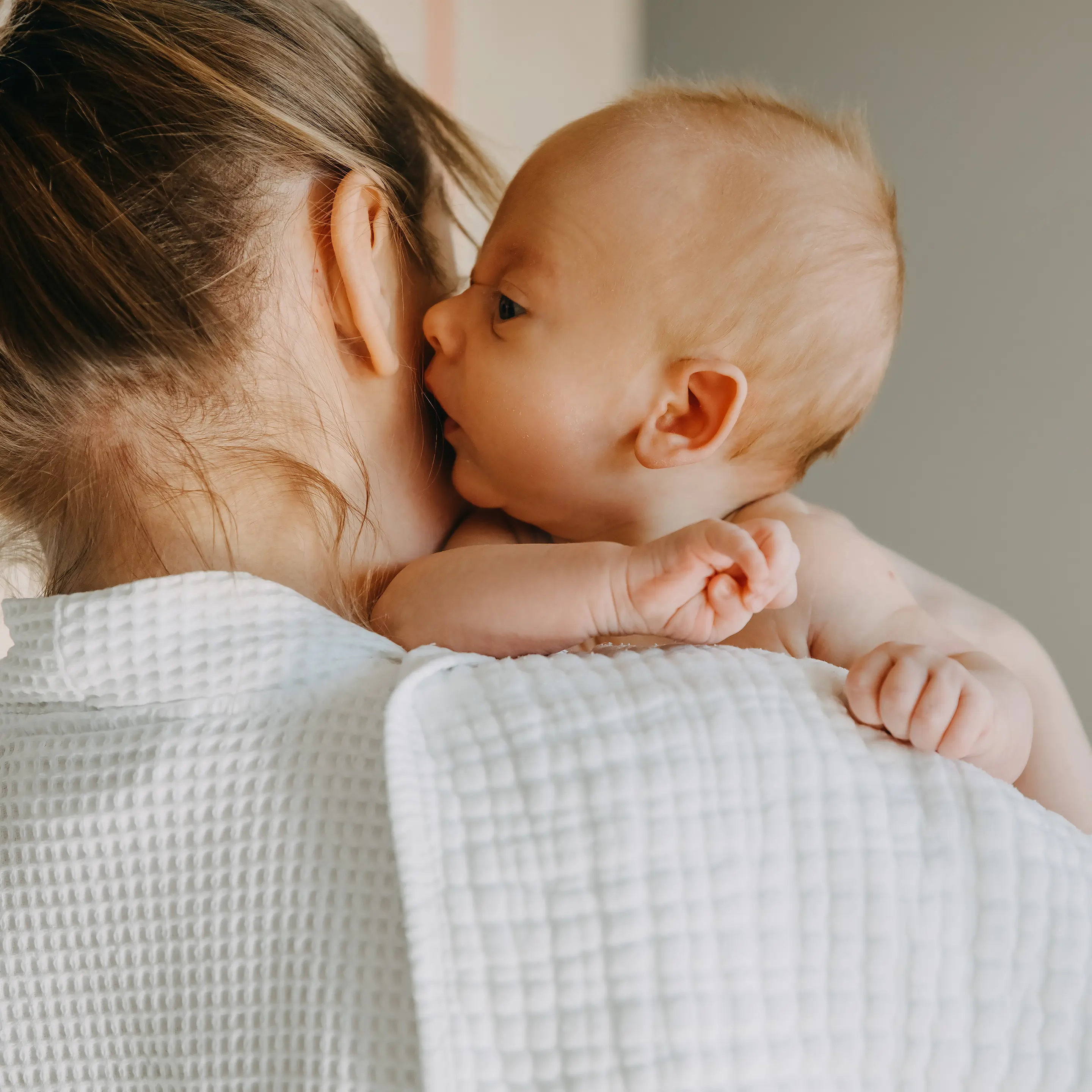 Mutter hält ihr Baby im Arm und trägt es nah am Körper.