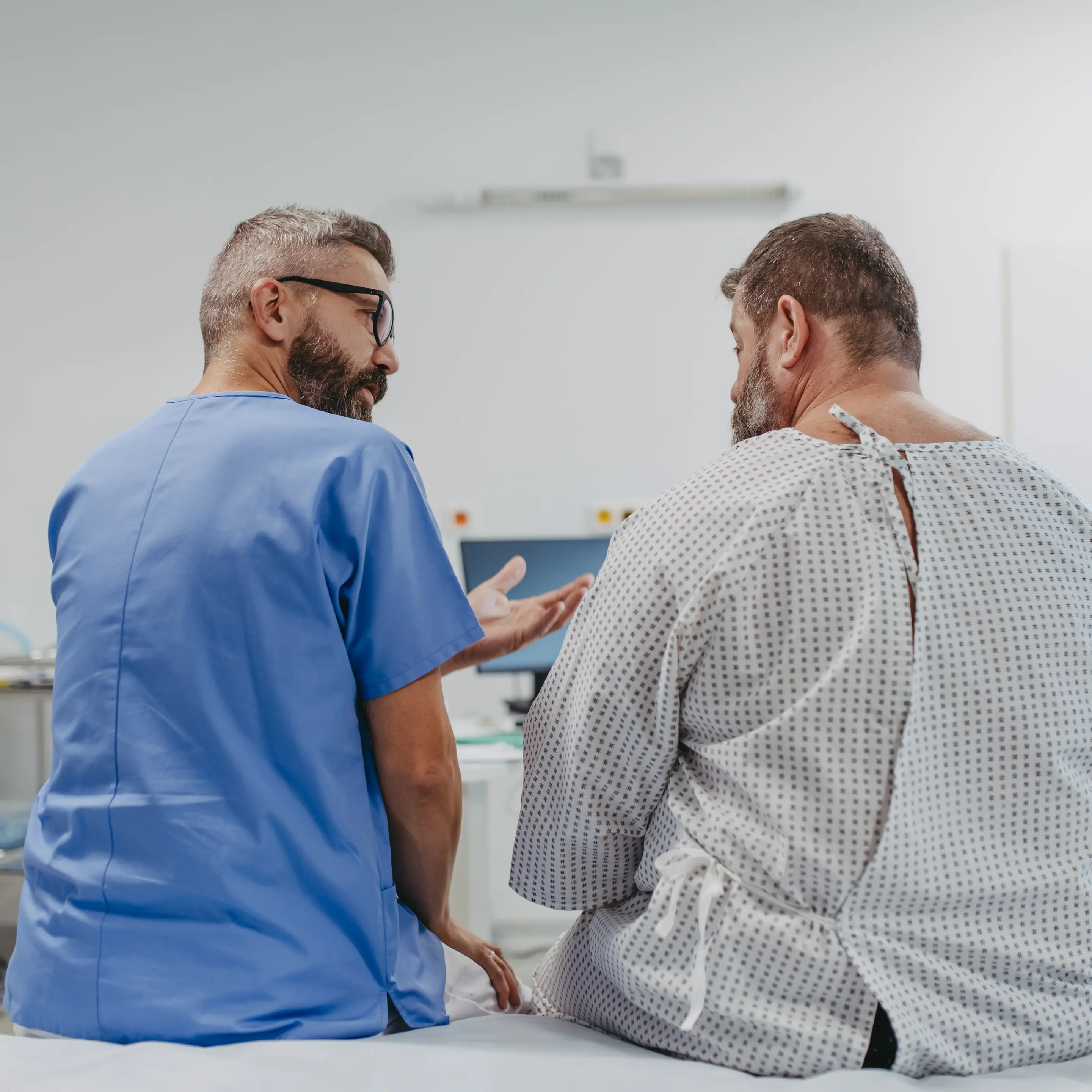 Eine medizinische Fachkraft sitzt neben einem Patienten und bespricht mit ihm eine Hämorrhoiden-OP.