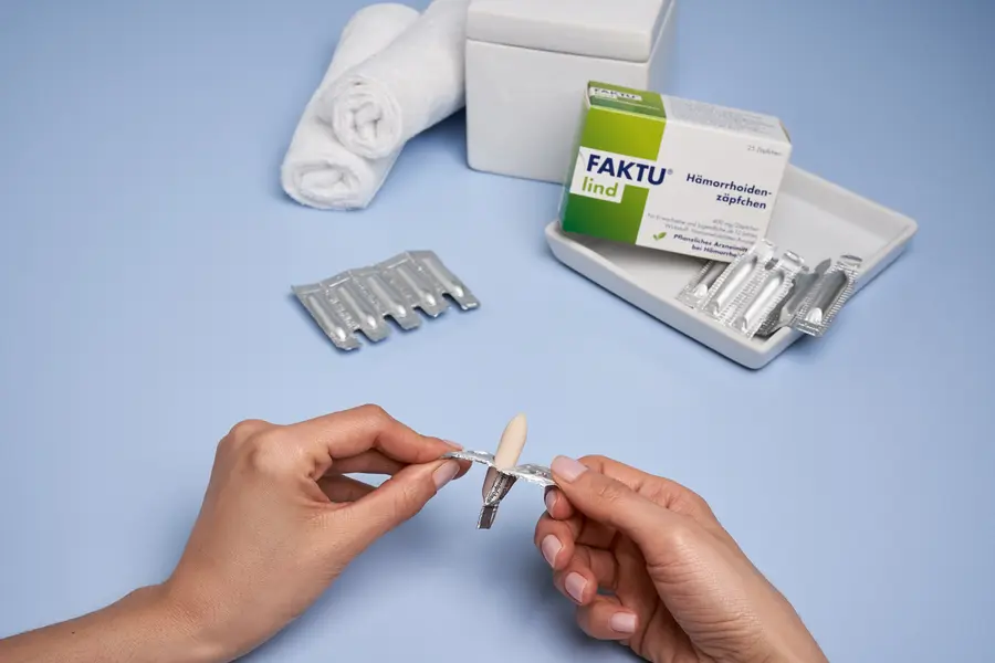 Person öffnet FAKTU lind Hämorrhoiden-Zäpfchen; im Hintergrund liegt die Verpackung.