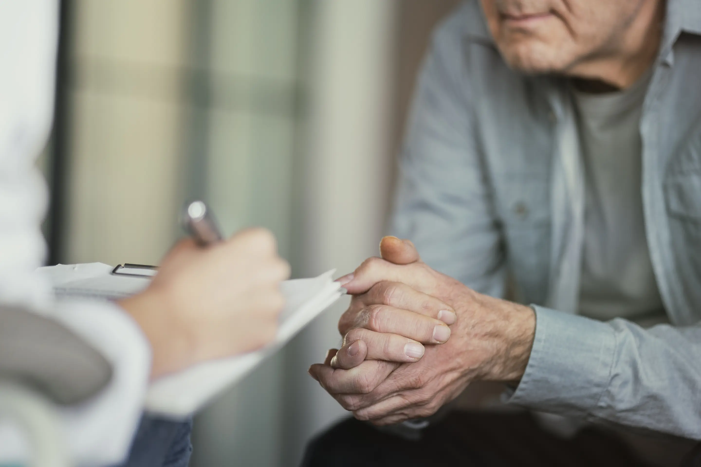 Ein älterer Patient im Gespräch mit einer medizinischen Fachkraft, die Notizen macht.