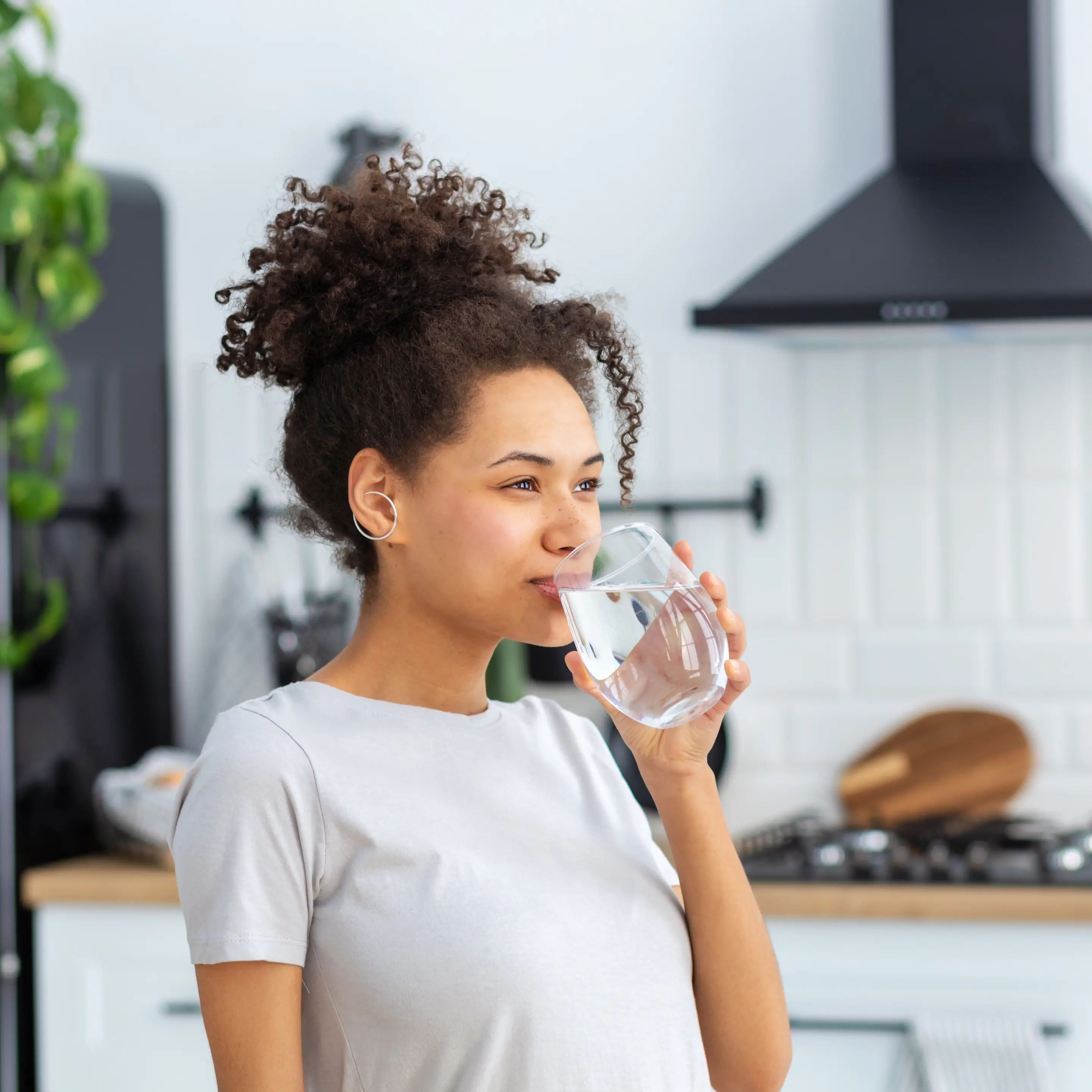 Frau steht in einer hellen, modernen Küche und trinkt ein Glas Wasser.