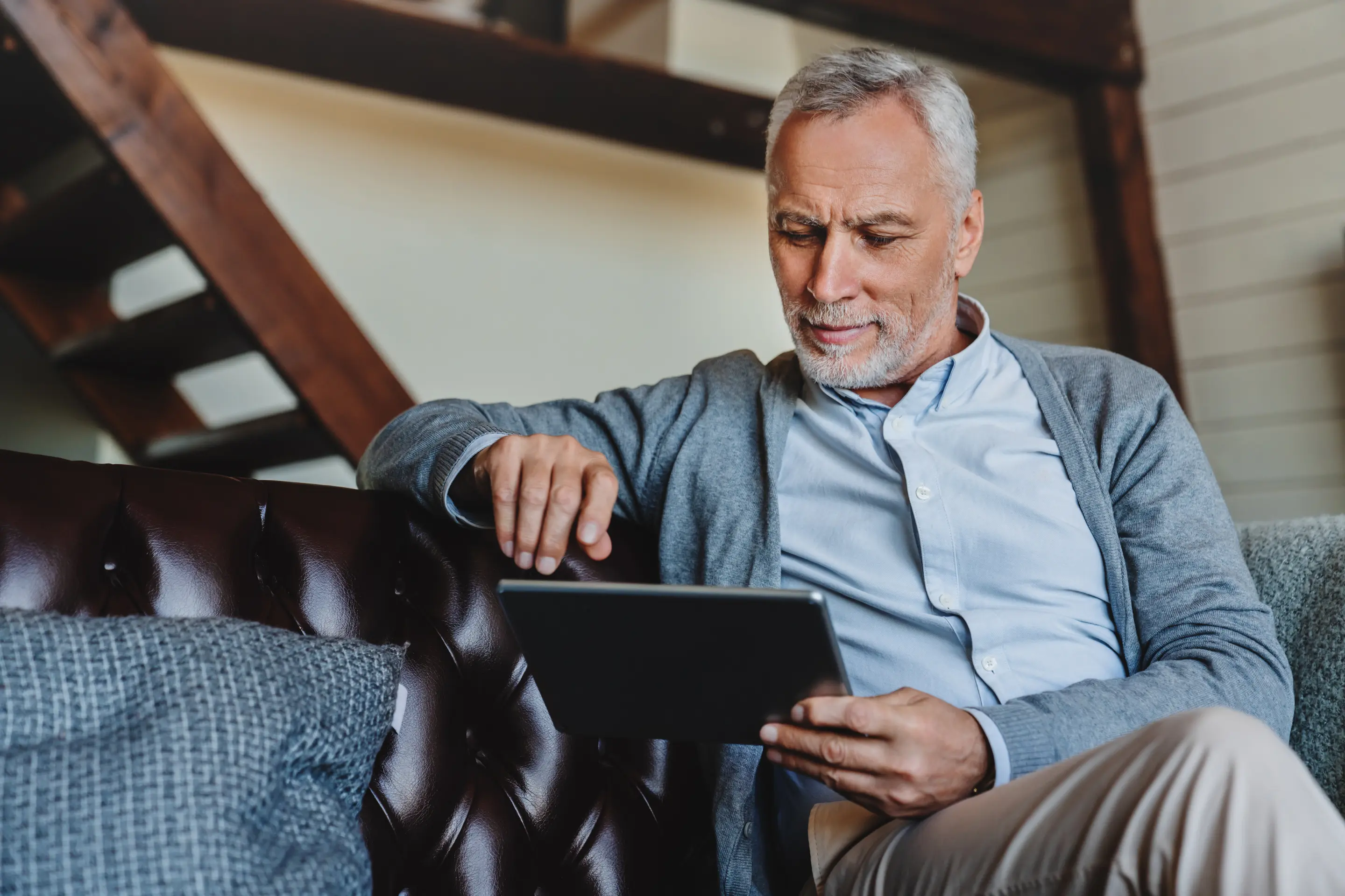 Ein älterer Mann sitzt auf einem Sofa und schaut auf ein Tablet.