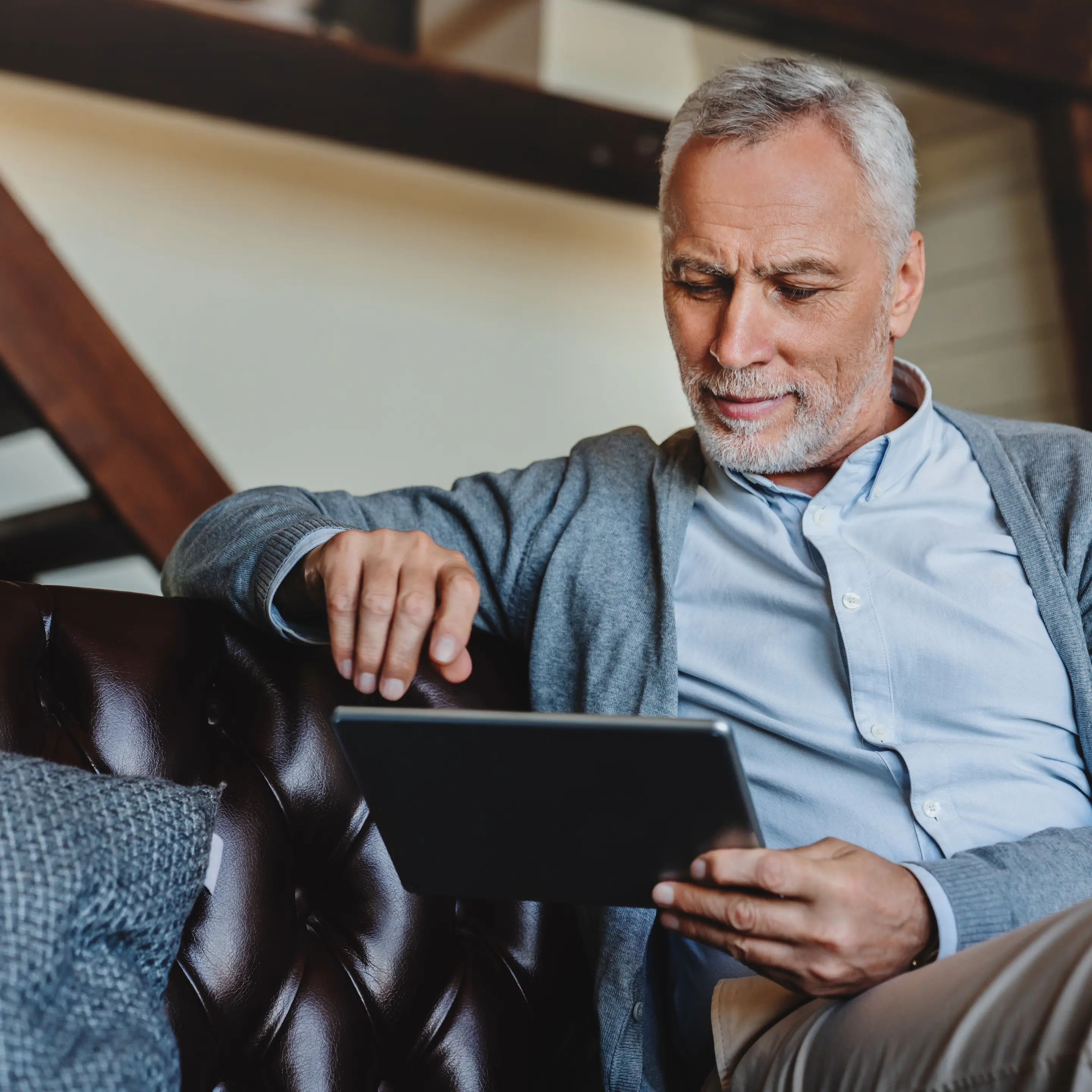 Ein älterer Mann sitzt auf einem Sofa und schaut auf ein Tablet.