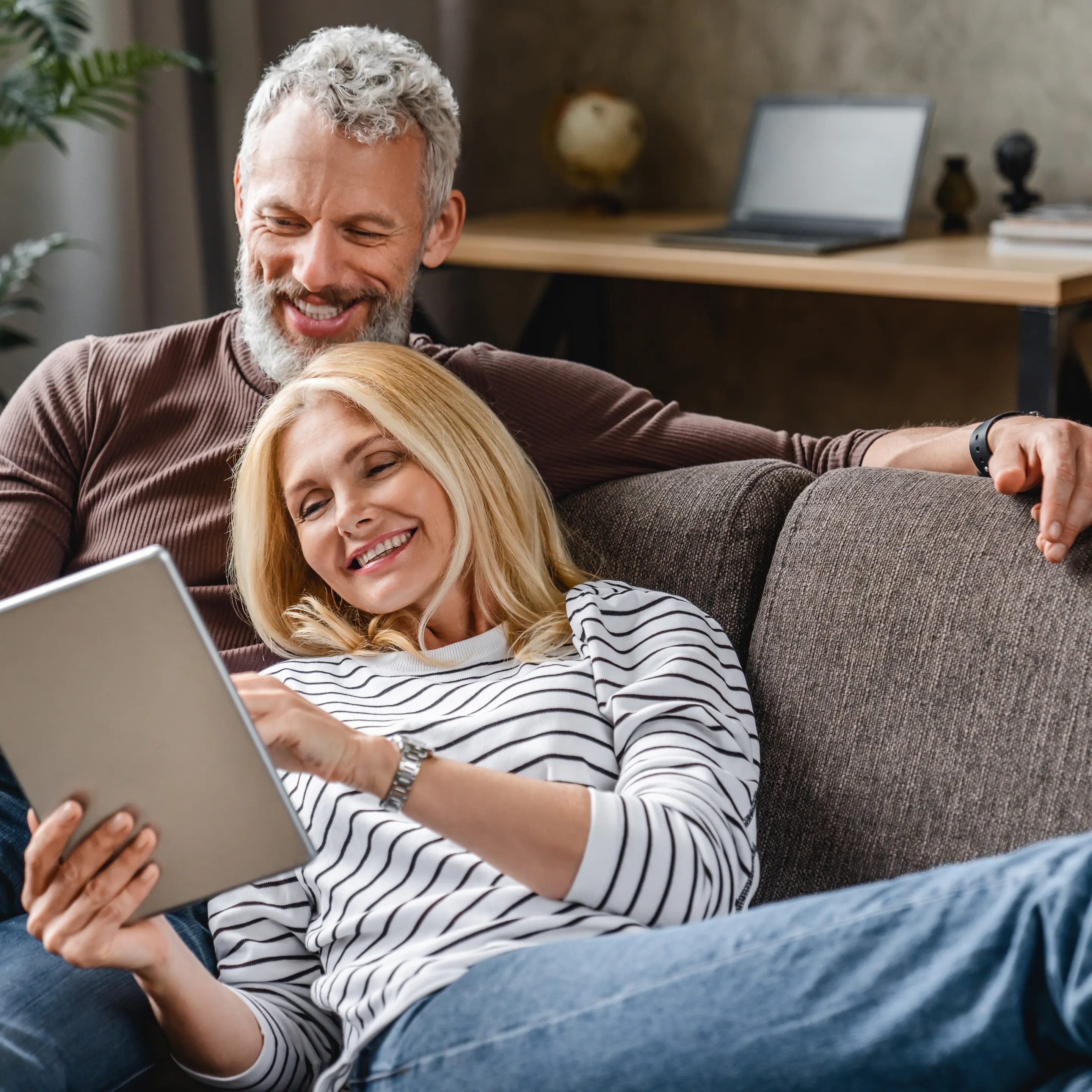 Lächelndes Paar entspannt gemeinsam auf dem Sofa und schaut auf ein Tablet.