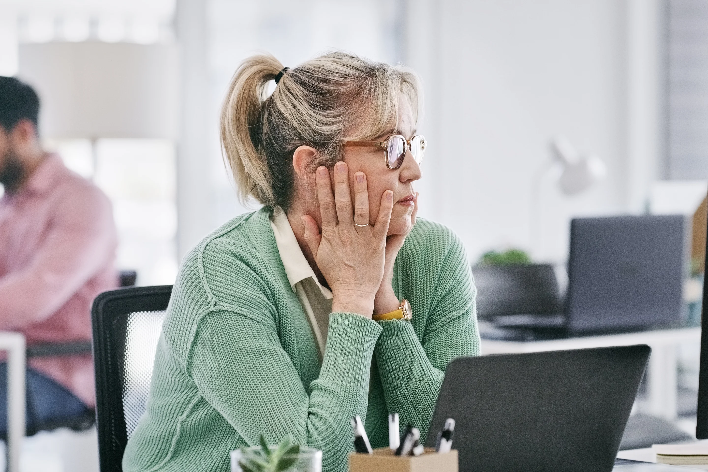 Eine Frau sitzt nachdenklich vor ihrem Computer im Büro.