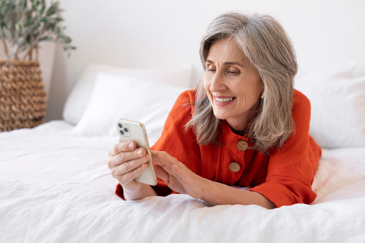 Smiling older woman using smartphone on bed