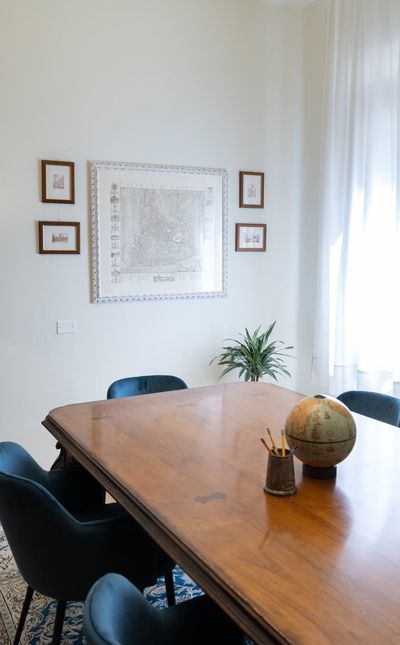 Elegant office with a wooden table, blue chairs, globe, pencil holder, plant, and framed maps on the wall, illuminated by natural light.