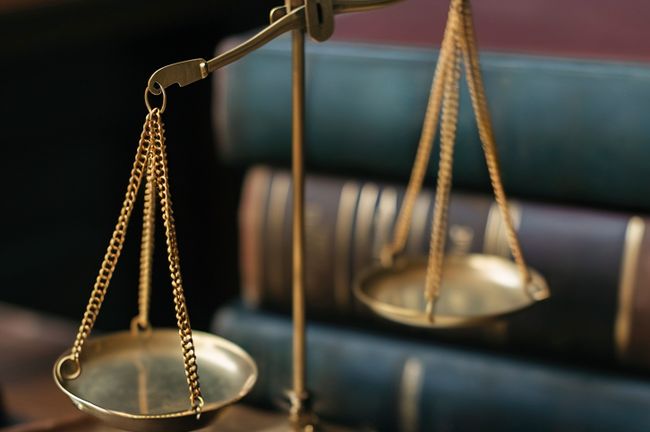A brass balance scale with chains, set against a background of stacked law books, symbolizing justice and legal matters.