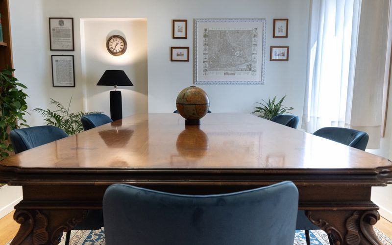 Elegant conference room with a wooden table, globe centerpiece, blue chairs, framed certificates, map on wall, and large window with sheer curtains.