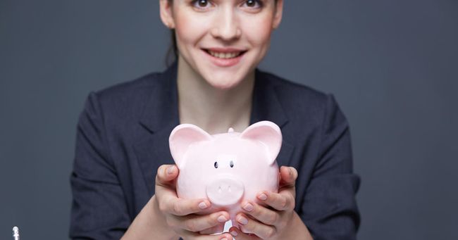 Smiling woman in suit holding a pink piggy bank, symbolizing saving and financial planning.