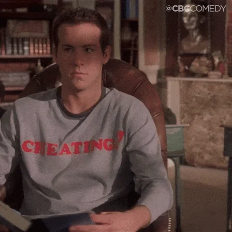A person seated in a chair wearing a shirt that reads “CHEATING.”