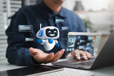 Person arbeitet an einem Laptop mit schwebender, lächelnder Roboterfigur und Chatfenstern in der Hand; AI-bezogenes Interface auf dem Bildschirm.